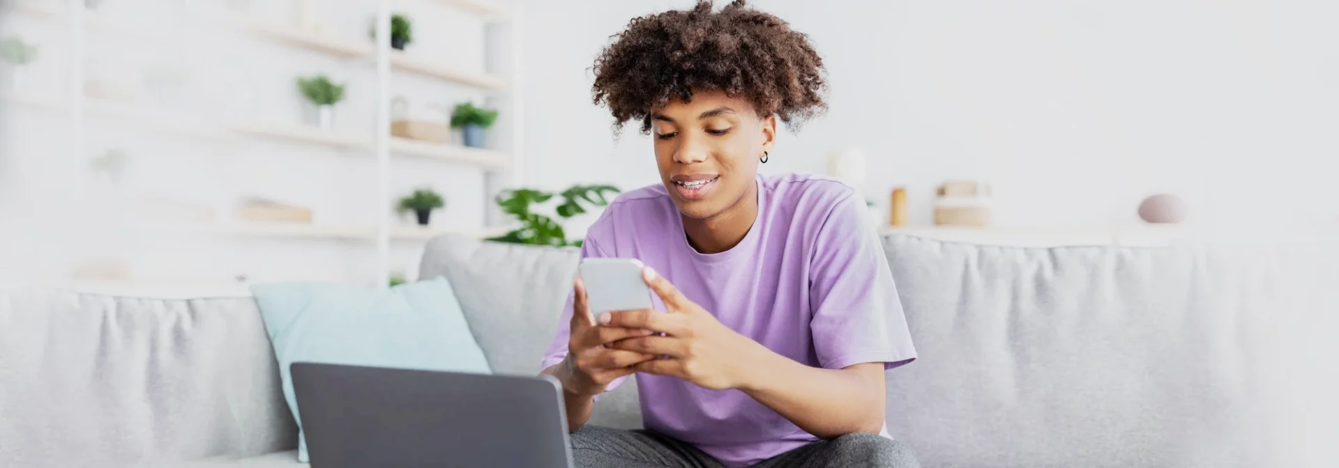 Happy young black teen in casual wear on smartphone and computer