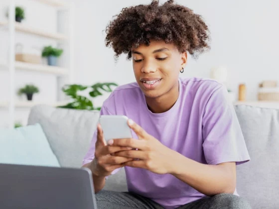 Happy young black teen in casual wear on smartphone and computer