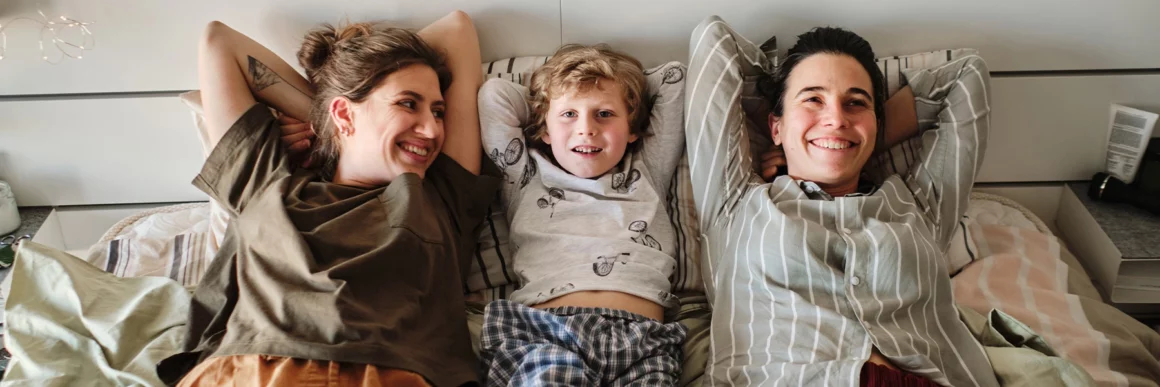 Young parents sitting on bed with young child smiling together