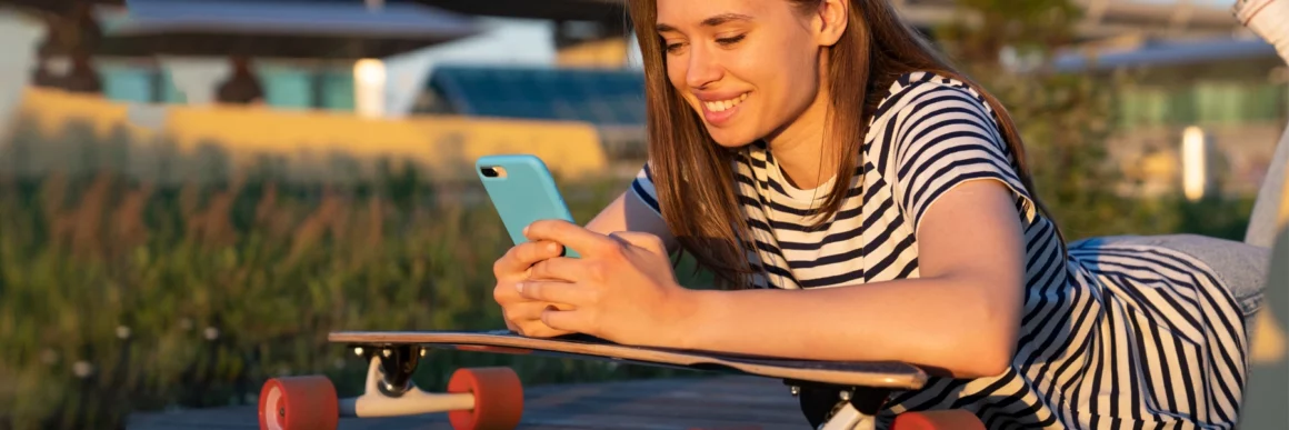 Teen girl smiling sitting outside with skateboard on her phone, teen on smartphone, social media