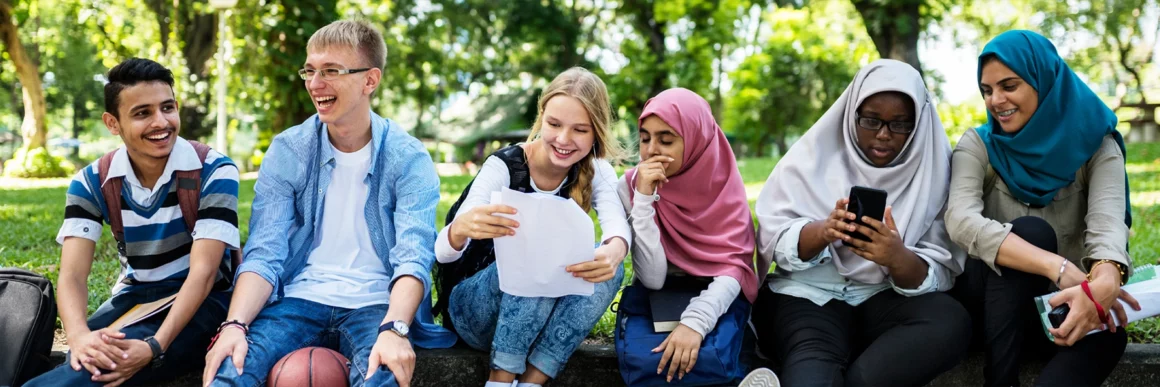 group of diverse teens sitting on curb together socializing