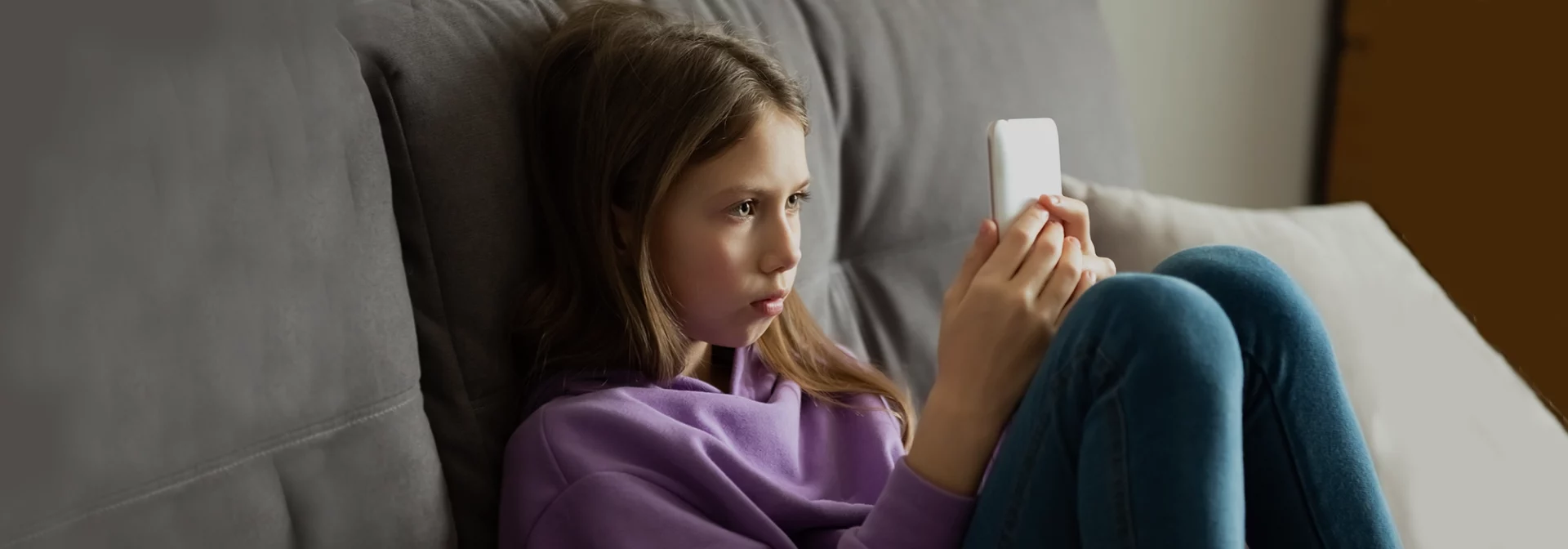 young girl with cellphone on couch looking at screen