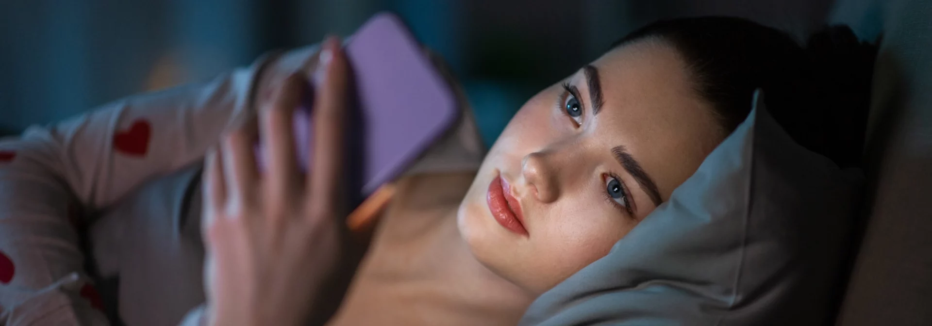 teen laying on bed in dark room on smart phone