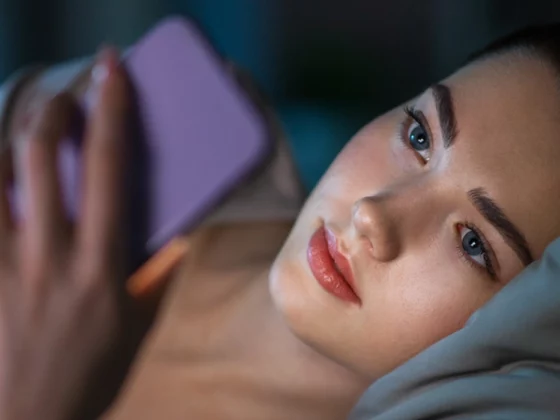 teen laying on bed in dark room on smart phone