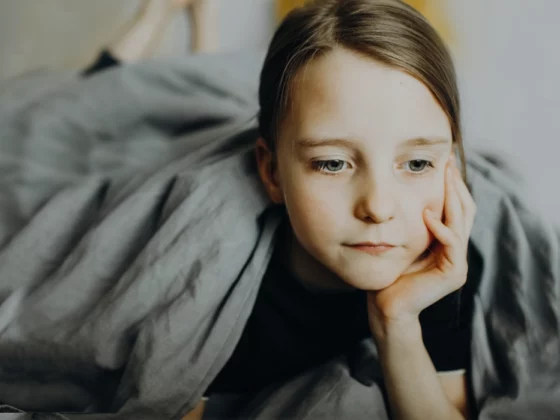 young girl sitting alone on bed looking sad