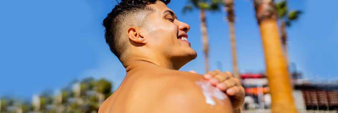 teen boy applying sunscreen to shoulder out in the sun